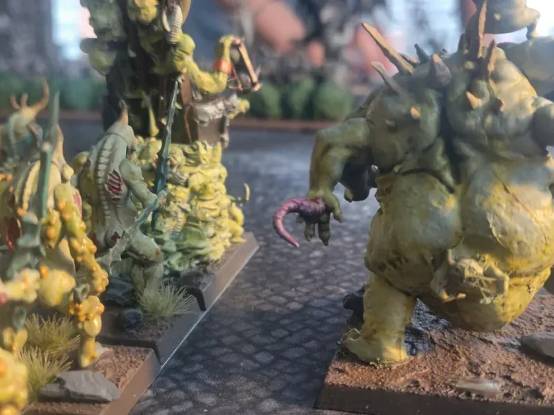Close-up of pale green Nurgle daemons advancing across a cobbled gaming table.