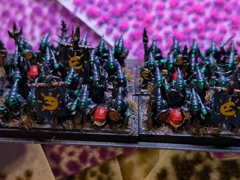 A hand holding a movement tray of painted 10mm Night Goblins in black robes with yellow moon-marked shields.