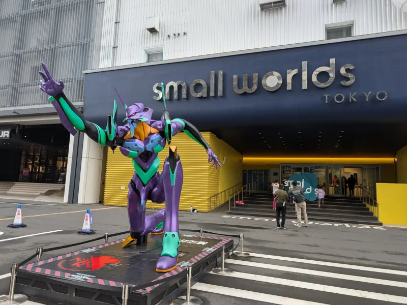 A life-size purple and green Evangelion statue kneeling outside the entrance to Small Worlds Tokyo.