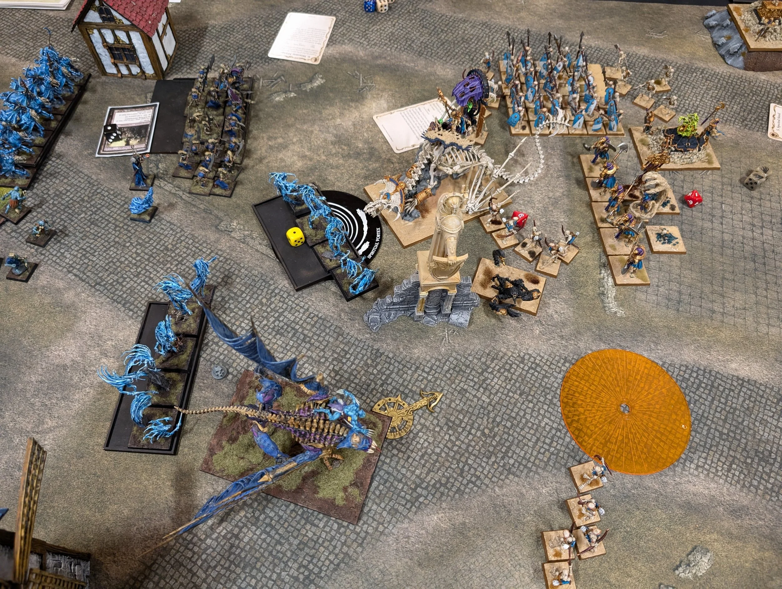Tomb Kings skeletons and a bone dragon meeting blue Vampire Counts spirit hosts and a winged Terrorgheist across a paved city table.