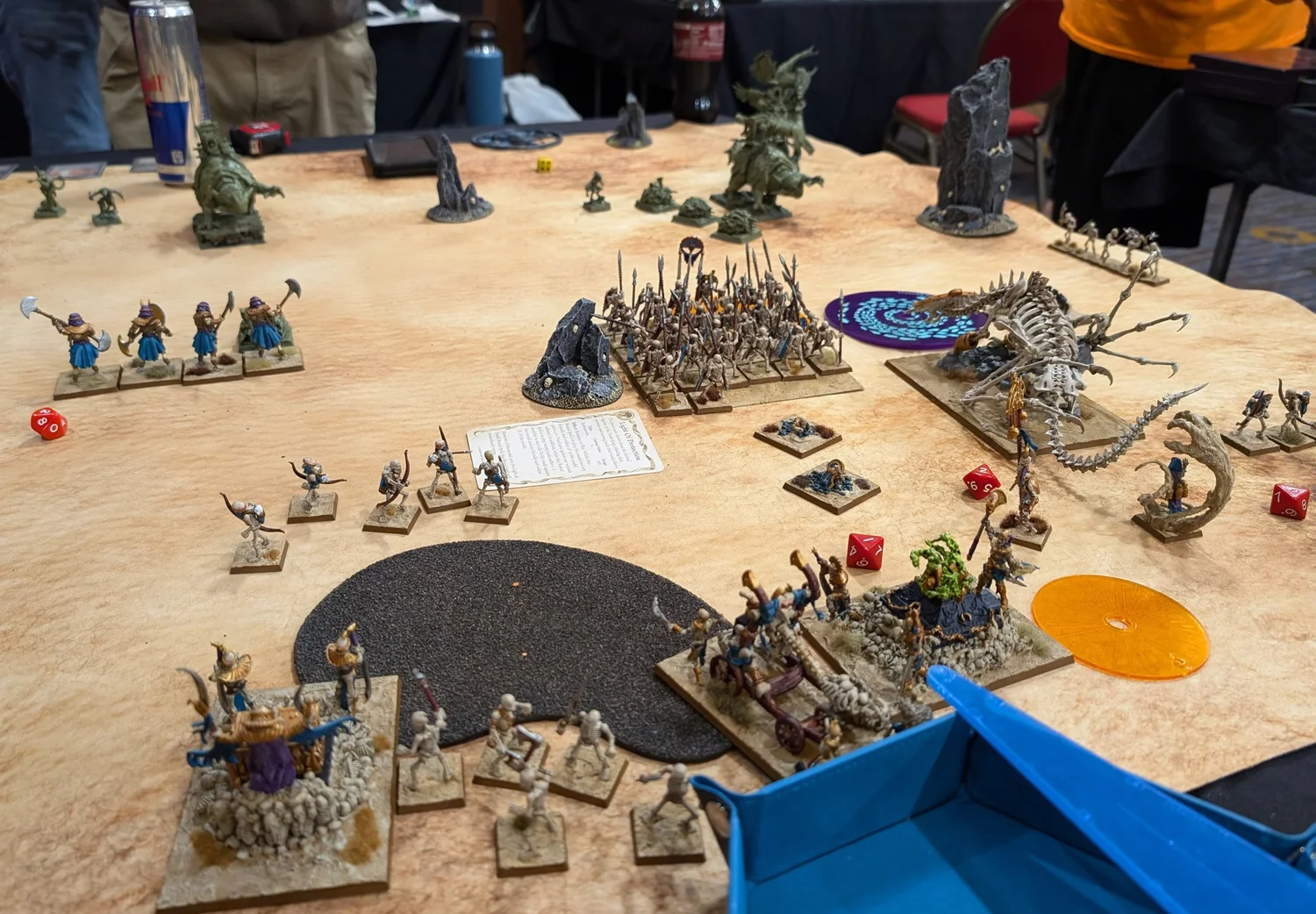Tomb Kings skeleton regiments and a bone dragon squaring off against green Lizardmen across a sandy tournament table.