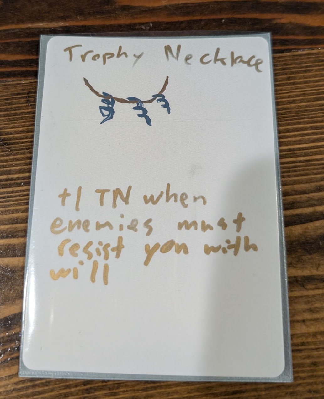 Handwritten Trophy Necklace item card with a necklace sketch and the rule: +1 TN when enemies must resist you with will.