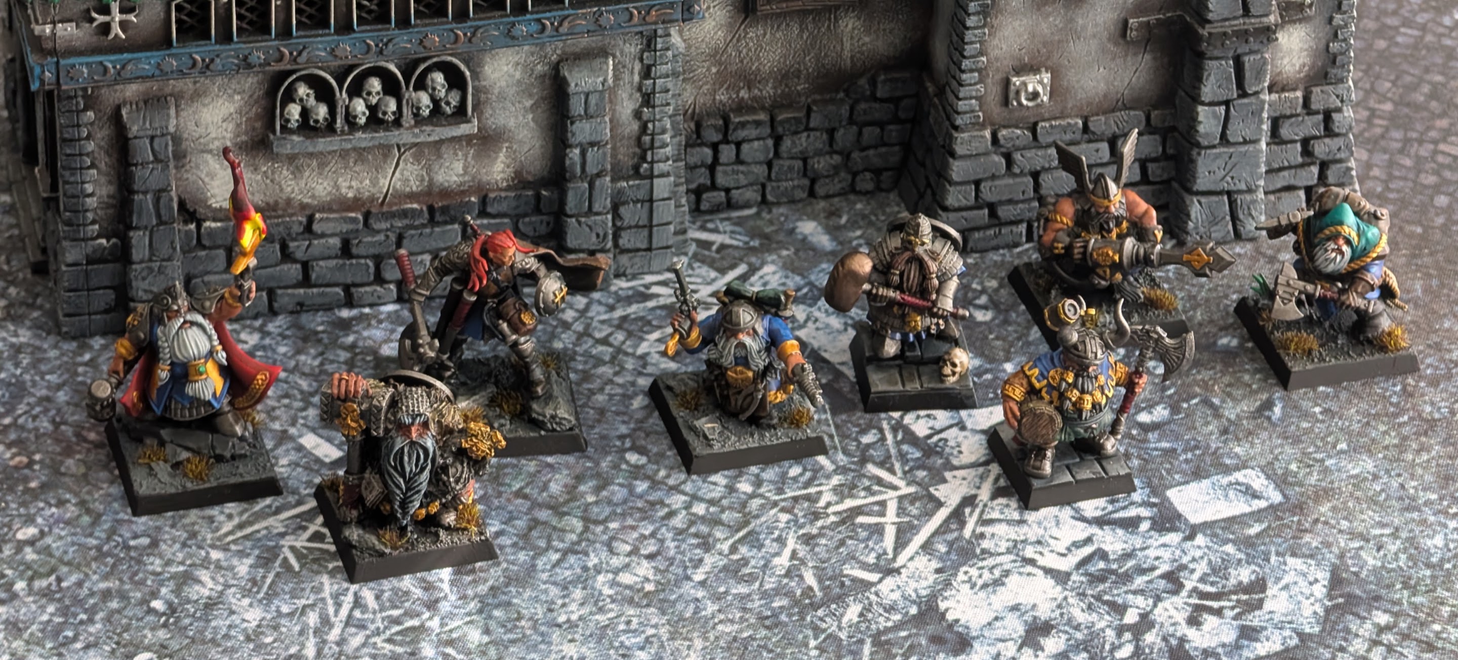 A lineup of painted dwarf hero and character models on a stone dungeon tile.